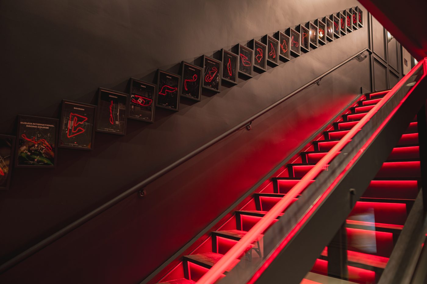 Red-lit staircase lined with framed Formula 1 circuit maps inside T11 Car Condo #303 at Circuit of the Americas